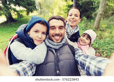 Technology, Travel, Tourism, Hike And People Concept - Happy Family With Backpacks Taking Selfie And Hiking