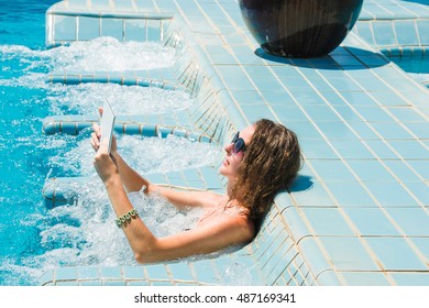 Technology and vacation concept. Luxury travel. Young pretty woman using tablet computer while relaxing in spa jacuzzi.