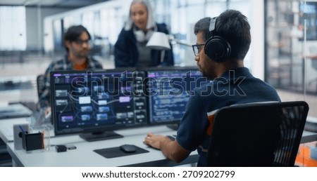 Tech-savvy Professionals Collaborating on Software Development in a Modern Office. Male Programmer Focused on Dual Monitors, Colleagues Discuss Project Strategies, Fostering Innovation and Teamwork.