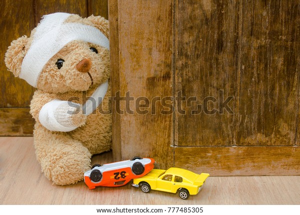 Teddy bear with bandages and\
toy car upside down on wood background with copy space,Accident\
concept.