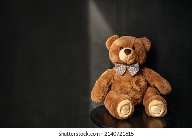 Teddy bear in a bow tie against the background of a chalk wall with rays of sunlight. Toy for children.
