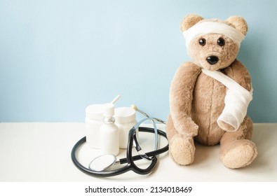 A teddy bear with a broken arm and a sore head sits on a blue background, there is medicine nearby and a fanidoscope lies.  The concept of children's medicine.  Banner place for copy text.