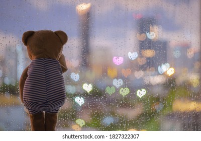 Teddy bear crying alone at window when raining with colorful love shape bokeh lights.