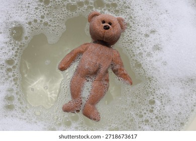 A teddy bear floating in soapy bubble water.
