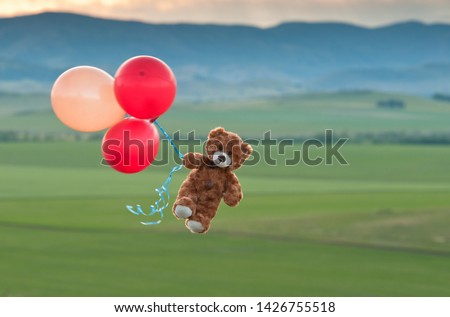 Teddy bear flying to the sky with a big yellow and red balloons.  A bear fly over the fields.  Pooh balloon travel. 