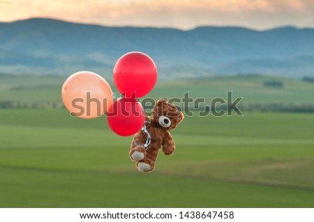Teddy bear flying to the sky with a big yellow and red balloons.  A bear fly over the fields.  Pooh balloon travel. Aerial travel. 