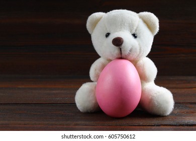 Teddy Bear holding an Easter egg, chicken, wood background.