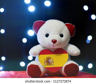 Teddy Bear Holding Spain Heart Shape Flag On Bokeh Background