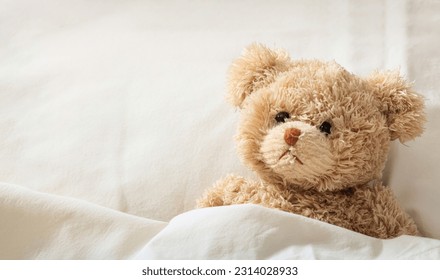 Teddy bear laying in bed on white sheets, closeup. Children healthcare concept