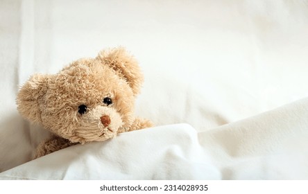 Teddy bear laying in bed on white sheets, closeup. Children healthcare concept