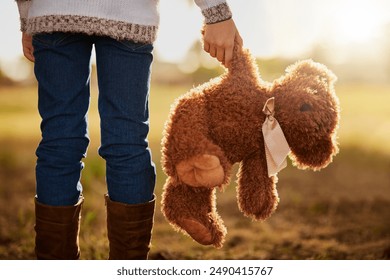 Teddy bear, legs and back of child in nature for support, fantasy and memory in field. Animal or toy, donation and lonely or orphan in countryside and walking or lost in park or outdoor for adoption