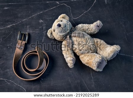 Teddy bear lies on the floor with leather belt, punishment. Parenting through domestic violence. Teddy bear symbolizing a child. The problem of child abuse.
