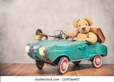 Teddy Bear And Old Leather School Bag Driving In Rusty Retro Turquoise Toy Pedal Car With Classic Brass Klaxon In Front Concrete Textured Wall Background. Vintage Style Filtered Photo