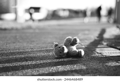 Teddy bear with sad face lying on footpath with blurry people,Image Black,White Lonely bear doll laying down on the road in gloomy day,Lost toy,Loneliness concept, International missing Children - Powered by Shutterstock