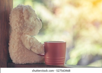 Teddy bear sits alone with red cup coffee with nature background