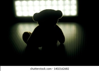 Teddy bear sitting lonely in the dark room.