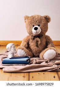A teddy bear sitting next to a stack of books, writing set and plaster bust