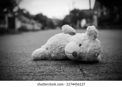 Teddy bear sleep on middle road with over light day and blur home. poster card for broken heart couple, sad, lonely, international missing Children, strong, gloomy day. alone unwanted cute doll lots.