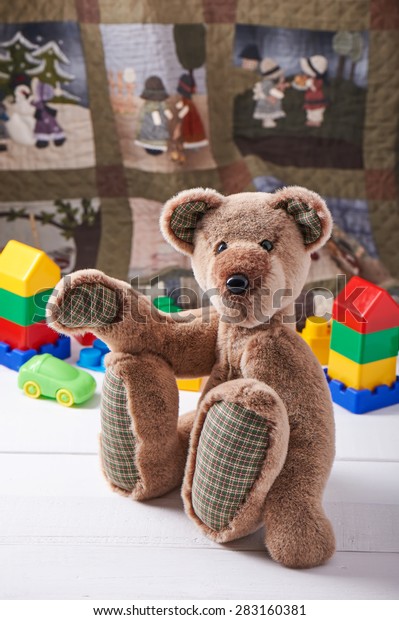 Teddy bear surrounded by blocks\
of children\'s plastic building kit on the background of the\
quilt