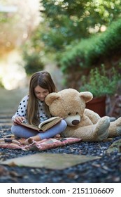 Teddy seems to be taking a nap from storytime. Shot of a little girl reading a book with her teddy bear beside her.