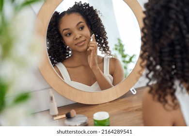 Teen African Mixed Race Girl Model Touching Healthy Smooth Face Skin Care Looking In Bathroom Mirror Applying Facial Cream. Teenage Beauty Skincare Morning Routine Concept.