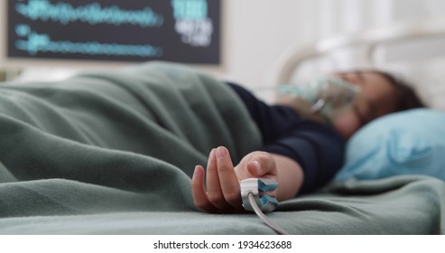 Teen asian girl in oxygen mask and oximeter sleeping in hospital bed. Portrait of unconscious child lying in bed and suffering from coronavirus in intensive care unit - Shutterstock ID 1934623688