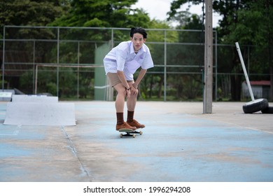 Teen Asian Skater Boy In Student Uniform Skating In The Local Skate Park. Young Sports Summer Action Concept.