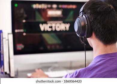 Teen Attending Online Electronic Sports Gaming Team Competition. Rear View. School Boy Wearing Headphone And Chat With His Teammate Through Microphone Over The Internet At Home Under Covid-19 Pandemic