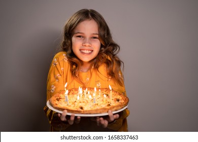 a teen blonde girl holding a pizza with candles is smiling on a white background. Original birthday.