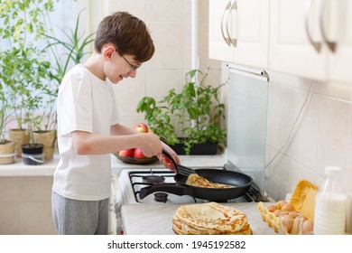 teen boy bakes (fries) pancakes in the kitchen. Cooking at home. Teenager boy is learning to cook. Kid boy 12 years old makes crepes by himself on frying pan. Independent child. Novice young chef - Powered by Shutterstock