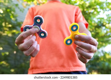 Teen boy with a fidget spinner sensory toys outdoors, shallow focus on fingers and spinner on the left