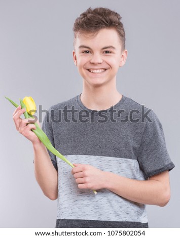 Teen boy with flower on gray background. Smiling child with tulip as a gift. Happy mothers, Birthday or Valentines day.