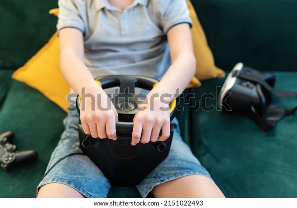 Teen boy gamer playing\
racing games on the computer. He uses the steering wheel. Getting\
ready for professional driving. Stimulation driving, child playing\
video game