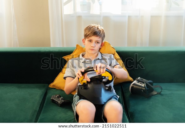 Teen boy gamer playing\
racing games on the computer. He uses the steering wheel. Getting\
ready for professional driving. Stimulation driving, child playing\
video game
