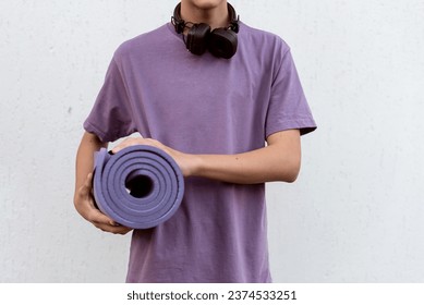 Teen boy with headphones holding yoga mat outdoor on white background. Child spending free time relaxing, sport, yoga, walking, listening music. Teen hobby, lifestyle and people concept - Powered by Shutterstock