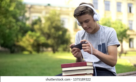 Teen Boy In Headphones Playing Mobile Game Instead Of Homework, Procrastination