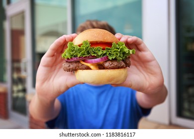 Teen boy holding a hamburger in front of his face