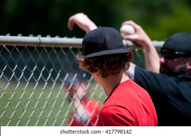 Teen Boy And Middle-aged Father Leaning On Fence Watching Baseball Game.