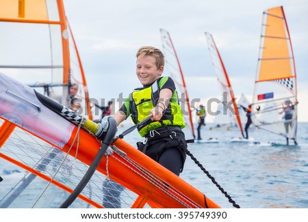 Teen boy raises windsurfing sail in the sea