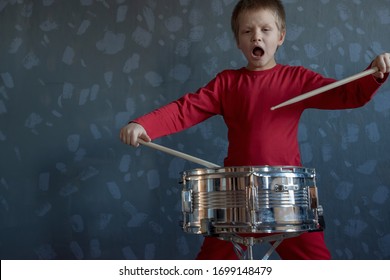 Teen Boy In Red Suit Playing Drum In Room. Child Holds Drumsticks