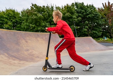 Teen boy rides stunt scooter towards the ramp on a skatepark. Concept of a healthy lifestyle and sports leisure