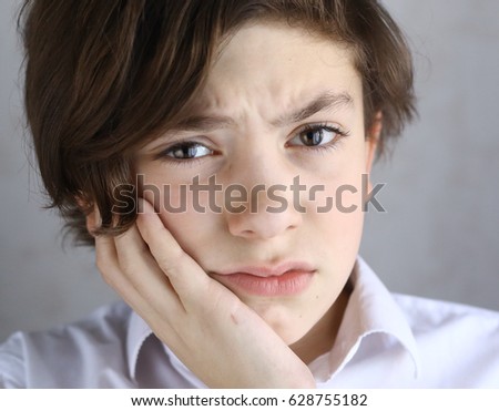 teen boy with toothache holding his cheek with palm