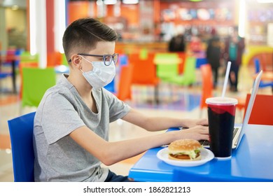 Teen Boy Wearing Face Mask Uses A Laptop In A Food Court