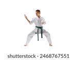 Teen boy in white karate and green belt demonstrating skills in stance, practicing isolated on white studio background. Concept of sport, martial arts, combat sport, healthy and active lifestyle