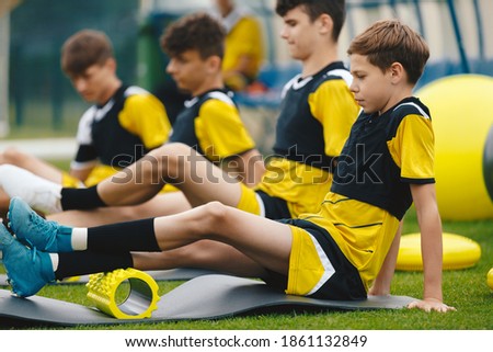 Teen Boys at School Soccer Stretching Session. Young Footballers Using Foam Rollers. Boys in a Soccer Team on Rolling Muscles on Grass Football Field
