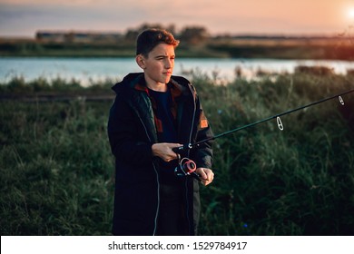 Teen Caucasian Boy Fishing With Father Stand On Pier. Sunset.