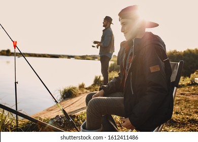 Teen Caucasian Boy Sit On Fishing Stool, Smile And Fish. The Sun Shine. Warm Day.