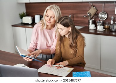 Teen Child Daughter Studying At Home In Kitchen With Mom. Teenage School Kid Girl Distance Learning Virtual Online Class With Mother Or Tutor Helping Doing Homework Together During Remote Education.