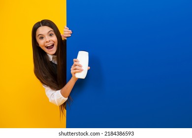 Teen child girl with shampoo bottle or shower gel isolated on yellow background. Kids hair cosmetic product. Excited face, cheerful emotions of teenager girl.