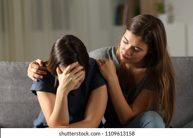 Teen comforting hes sad friend in the night sitting on a couch in the living room at home